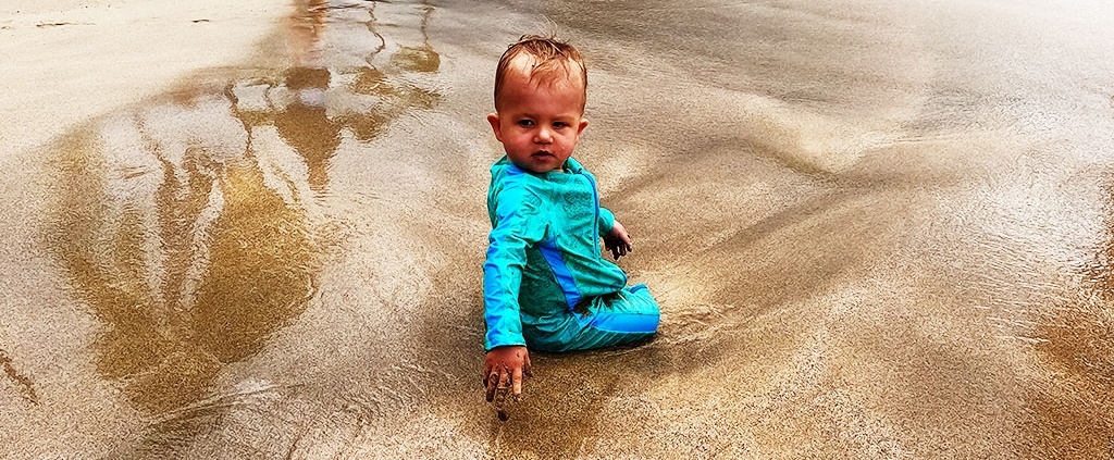 Baby sitting on the beach at kids swim lesson. How early should Hawaii swimming lessons start, is answered by Salty Swim School.